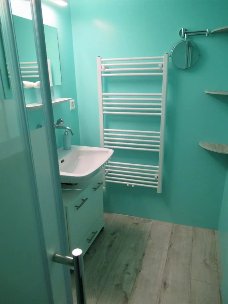 Badezimmer in Türkis mit Waschtisch, Spiegel, Handtuchradiator und Dusche.