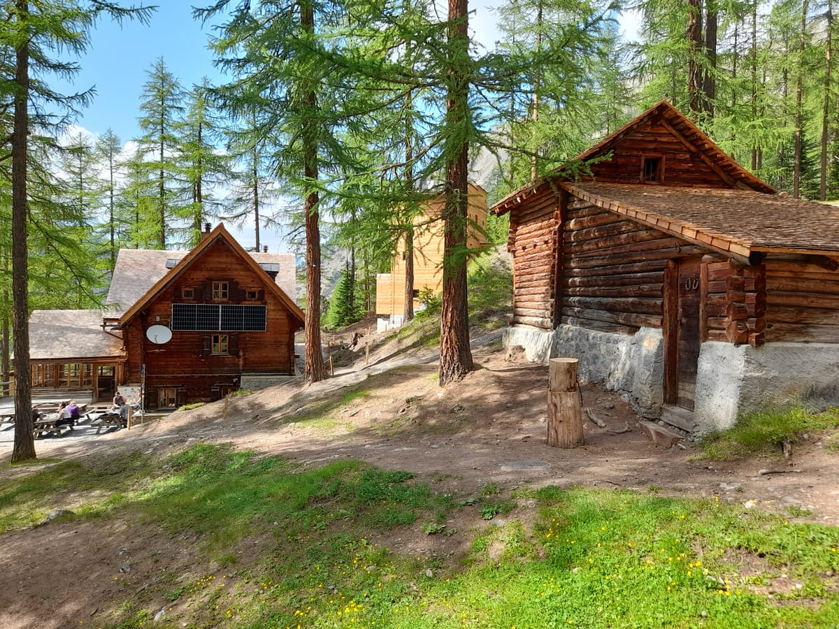 Die Cluozzahütte im Schweizerischen Nationalpark zwischen Lärchen, rechts ein alter Blockbau.