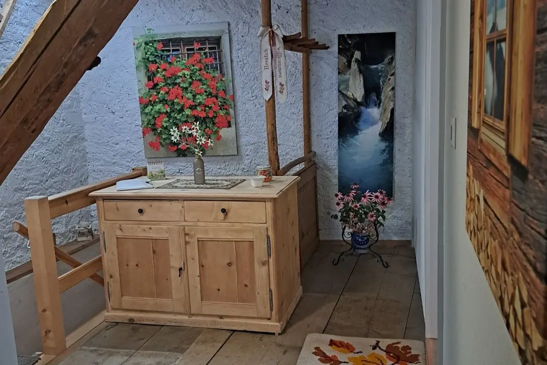 Gang im Dachgeschoss unter Holzbalken, mit einem Waschtisch aus Holz und einem Blumenbild an der Wand.