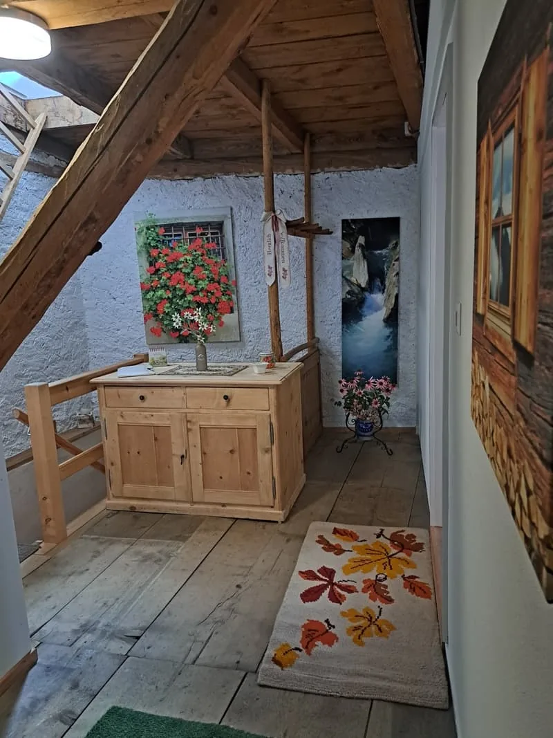 Gang im Dachgeschoss unter Holzbalken, mit einem Waschtisch aus Holz und einem Blumenbild an der Wand.
