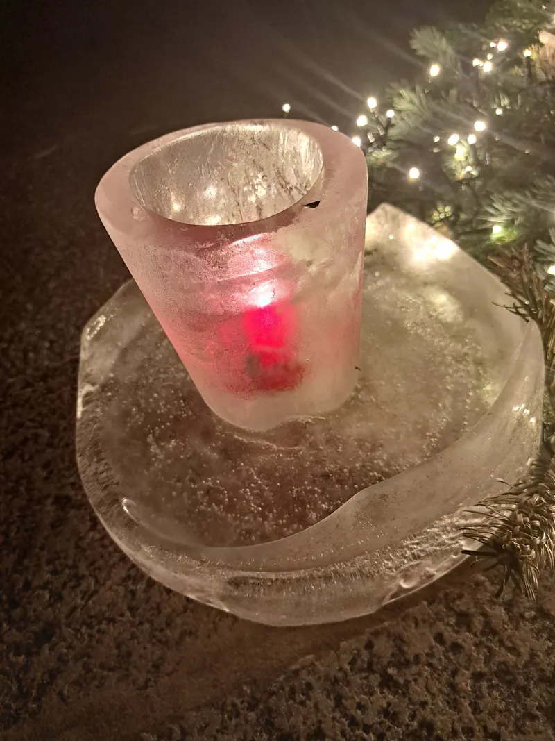 Eislaterne mit einer roten Kerze, daneben ein Tannenzweig mit Lichterkette.