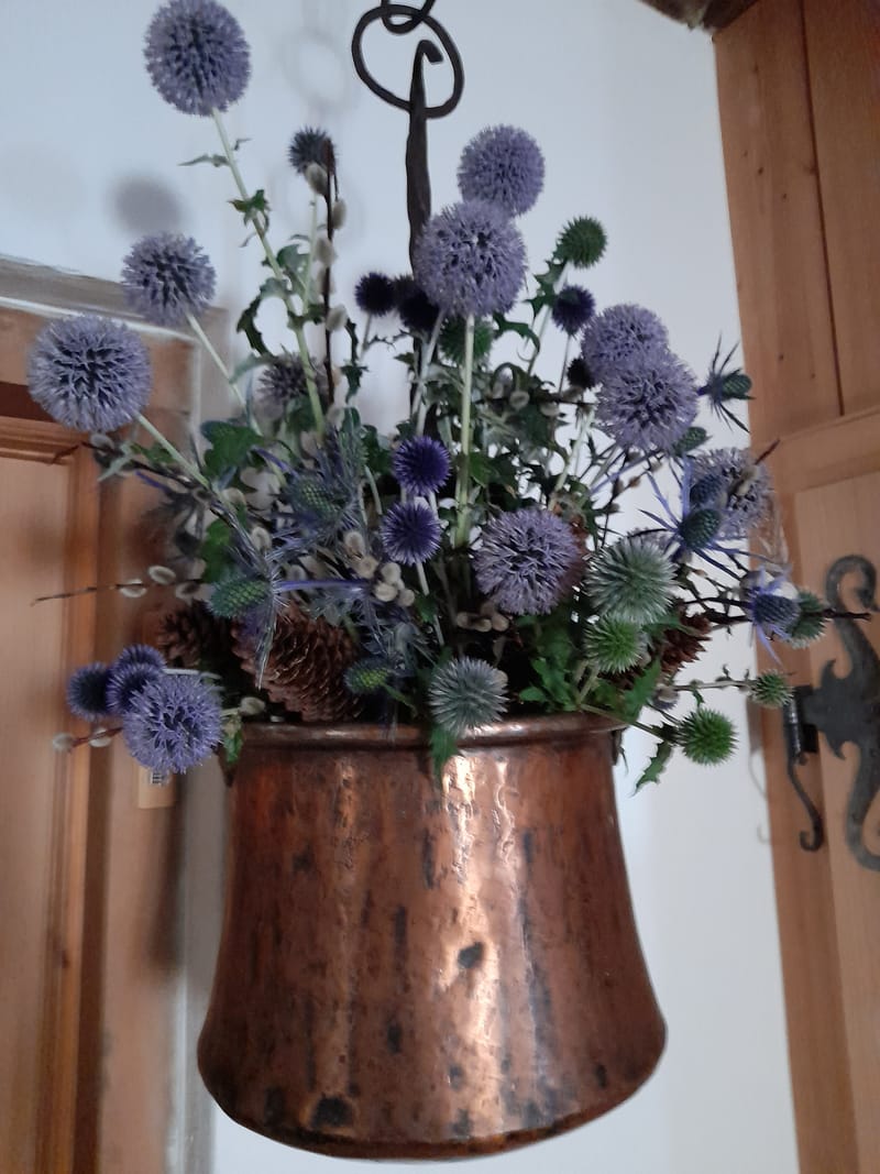 Aufgehängter Kupferkessel mit blauen Kugeldisteln, Weidenkätzchen und Tannzapfen.