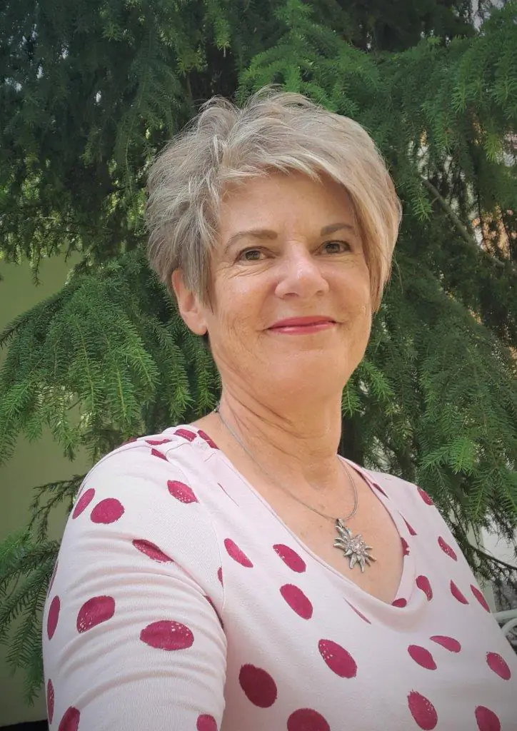Marina Margadant, Gastgeberin der Engadin Auszeit, im Garten vor einem Nadelbaum.