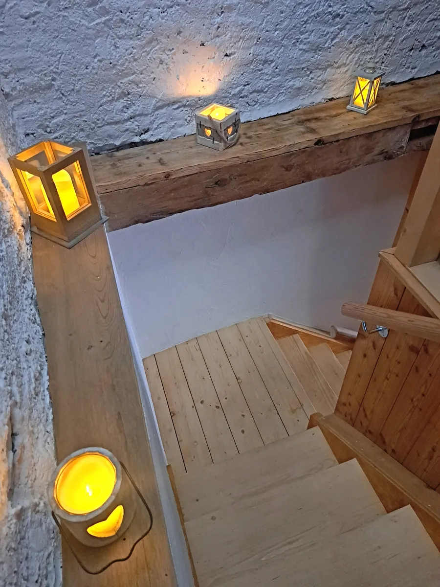 Das Treppenhaus am Abend: auf dem Balken und der Wand brennen mehrere Laternen und Windlichter.