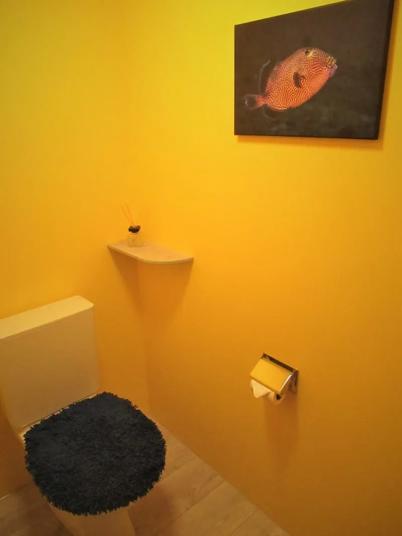 Separates WC mit gelben Wänden, einer Eckkonsole mit Trockenblumen und einem Bild an der Wand.